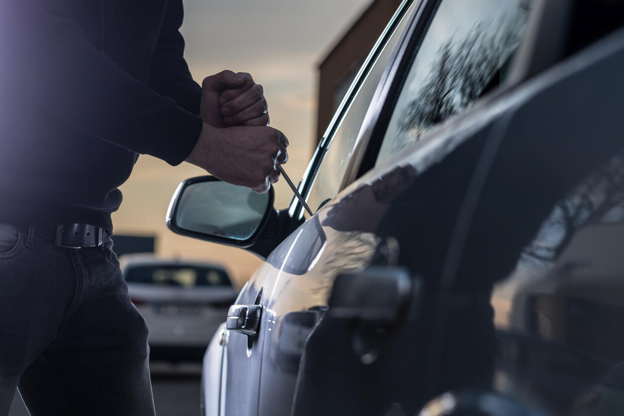 A person using a tool to break into a car door, symbolizing a possession of a stolen vehicle charge and the need for a criminal defense lawyer.