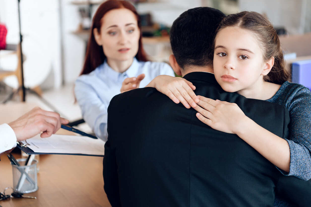 A child hugging a parent, with another parent and lawyer discussing documents in the background, symbolizing child support proceedings.