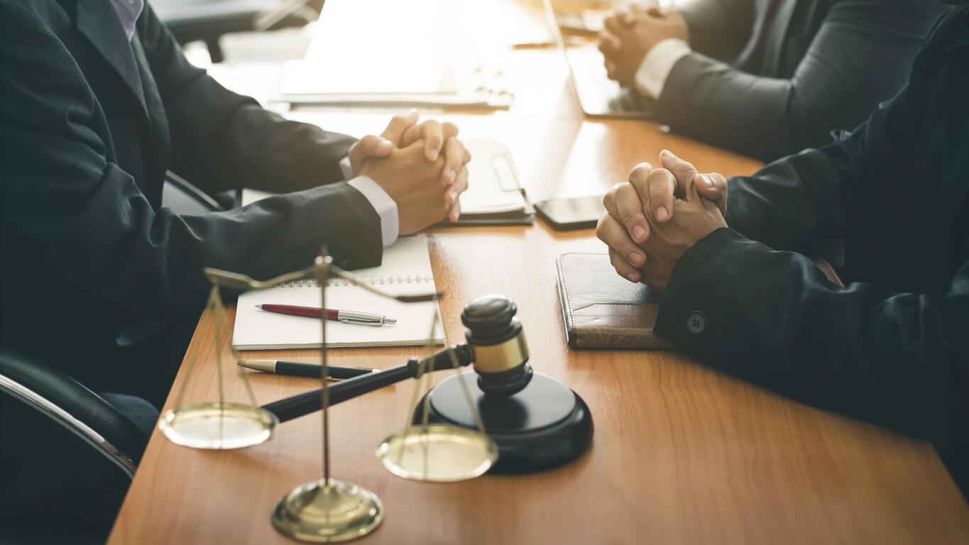 Gavel and scales of justice on a table during a mediation session with attorneys and clients, representing the process of legal dispute resolution.
