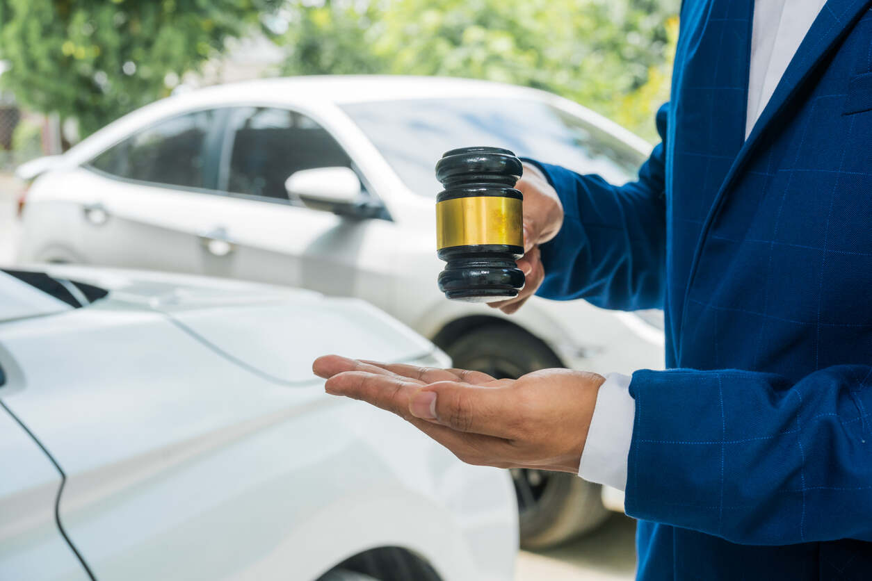 A lawyer holding a gavel in one hand and gesturing with the other, standing next to a car, symbolizing a car accident claim.